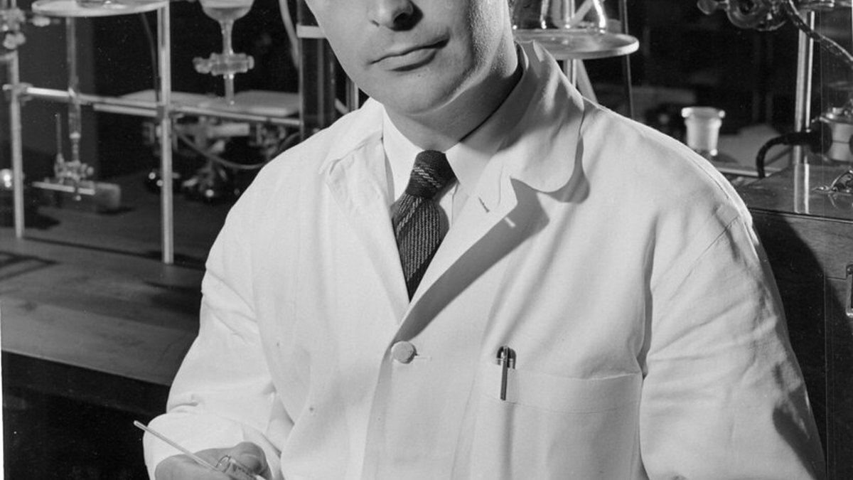 A mid-century research laboratory with a scientist in a white coat at a bench of glassware — the patient bench chemistry through which gut and islet appetite hormones such as PYY (peptide YY) and amylin were isolated, a Panacea Bio Chem reference by Bogdan Dicoias